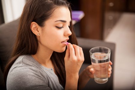 mladá žena berie antikoagulačné lieky a zapíja ich pohárom vody