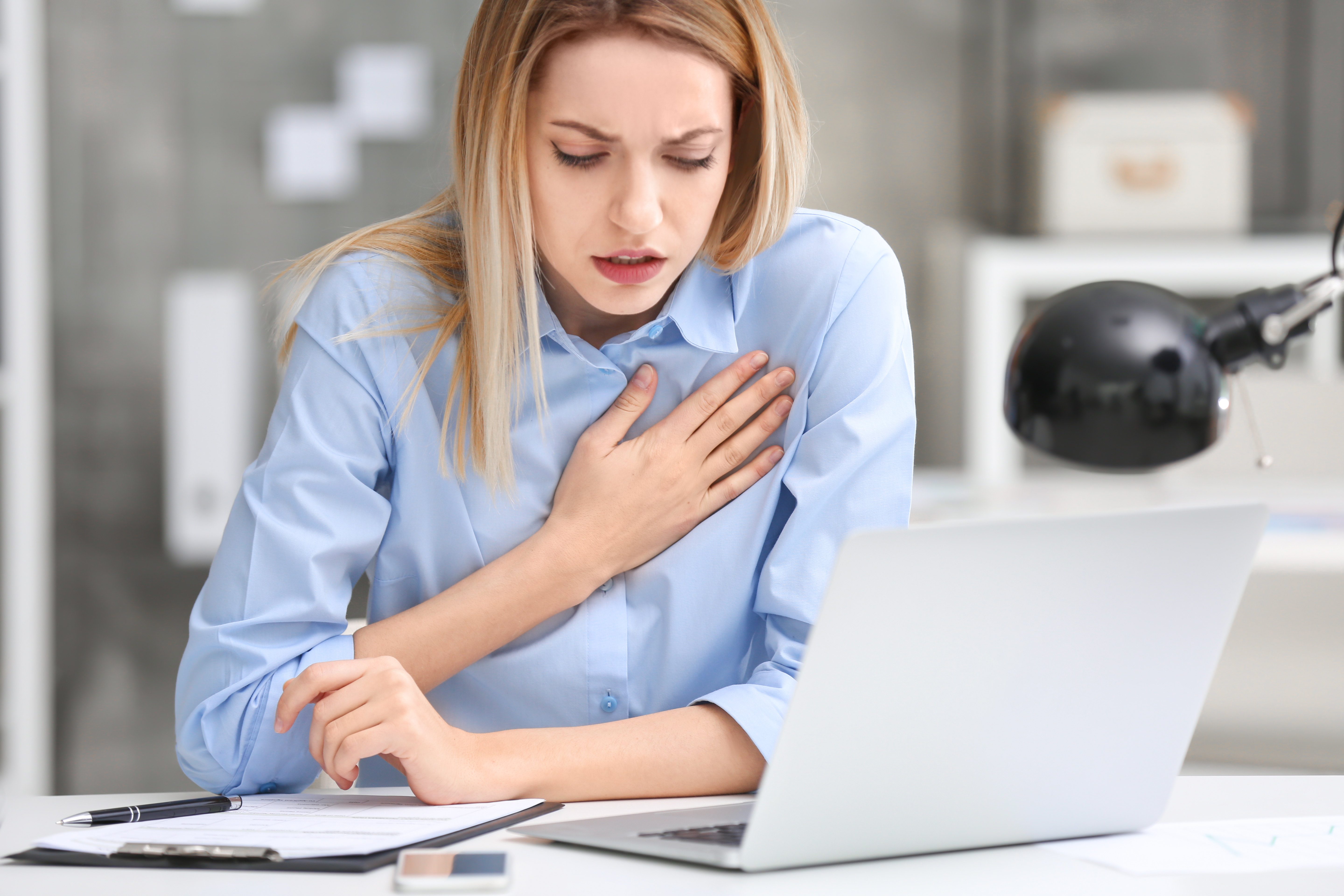 Mladá žena za notebookom sa s bolesťou chytá za srdce