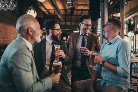 Skupinka štyroch mužov sedí v bare, pije pivo a zabáva sa