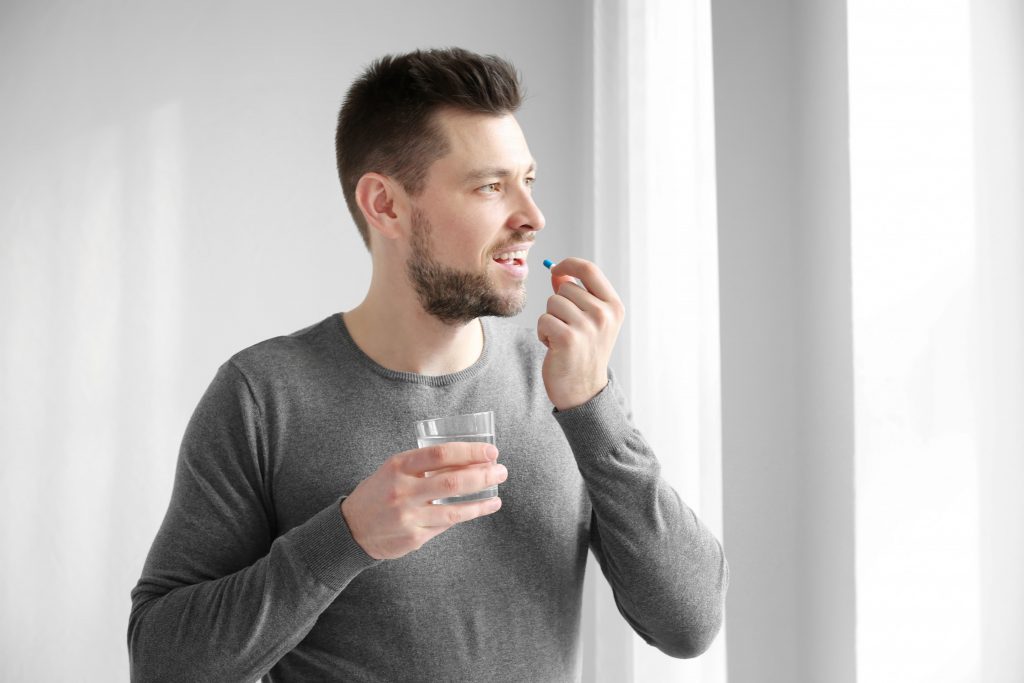 muž si dáva tabletku a zapíja ju pohárom vody