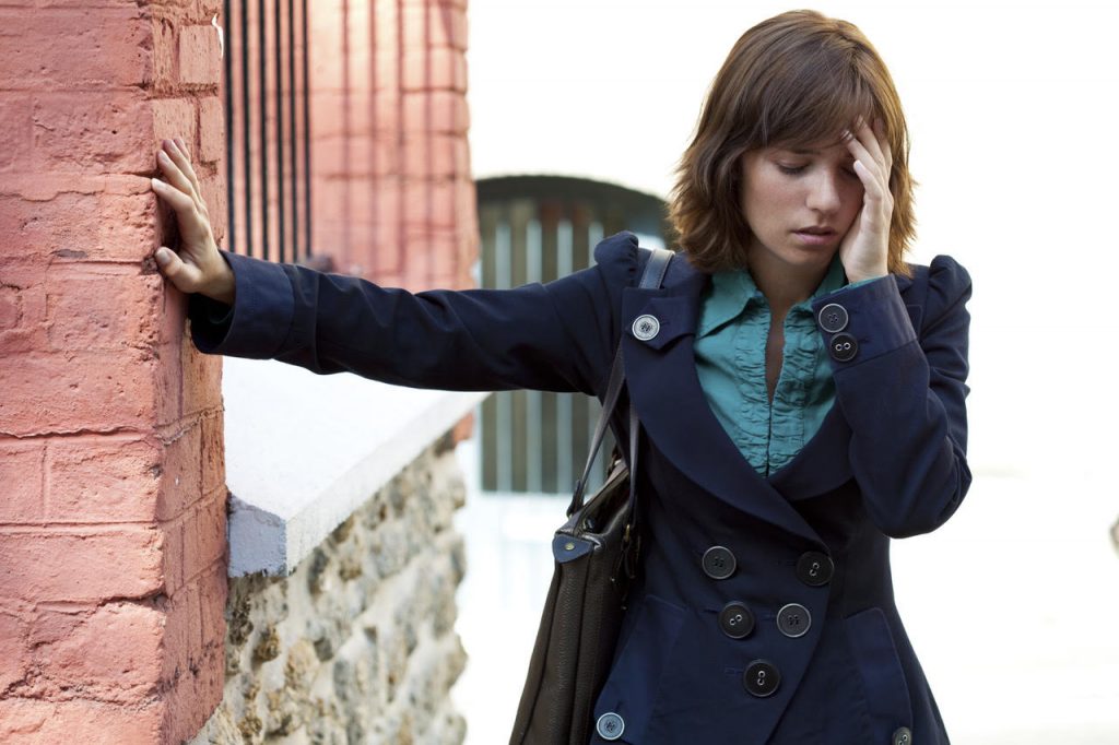 mladá žena sa opiera o stenu a drží za bolestivú hlavu